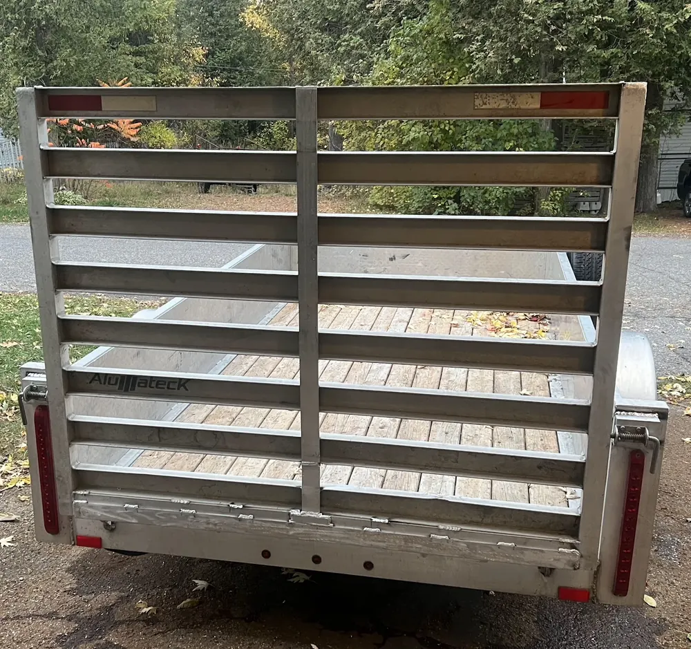Straight-on view of an aluminum trailer tailgate with horizontal bars, welded seams along its bottom edge